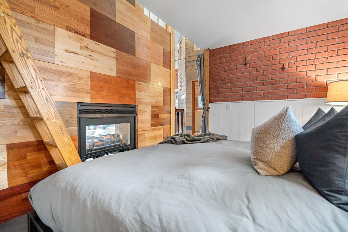 A bedroom with a sloped ceiling, a fireplace, and a brick wall.
