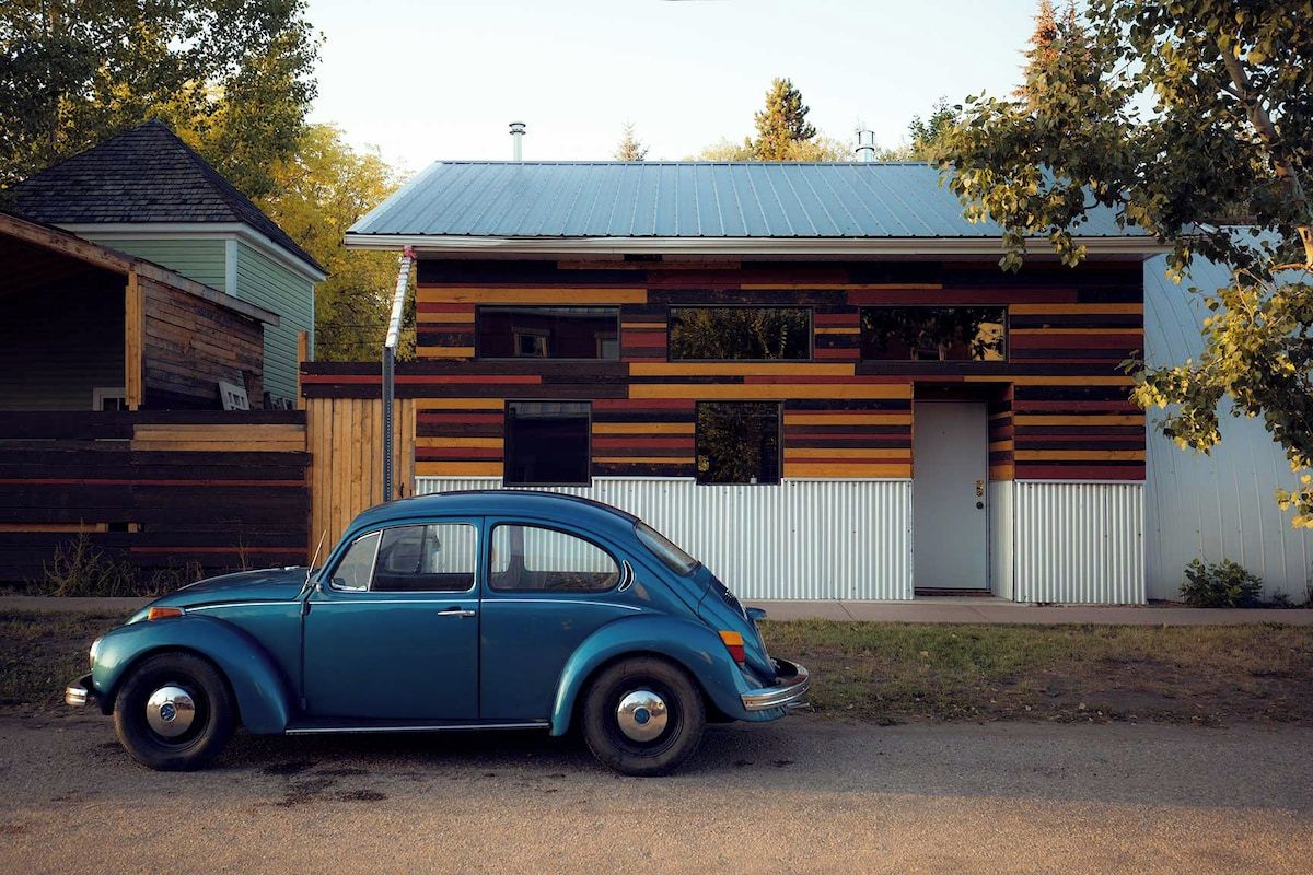 Ein Oldtimer vor einem modernen Haus mit geneigtem Dach und horizontalen Holzpaneelen.