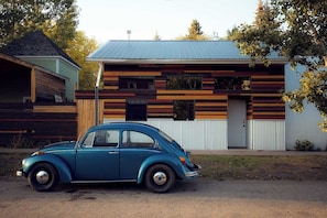 A vintage car parked in front of a modern house with a sloped roof and horizontal wooden panels.