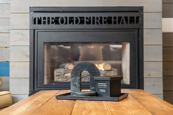 A fireplace with a stone arch decoration and a whiskey candle holder on a wooden table. - Historic Firehall Guesthouse with Private Covered Patio & Wood Stove (Rosebud)