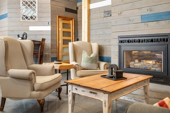 A cozy room with a fireplace, two armchairs, a wooden table, and a ladder against the wall.