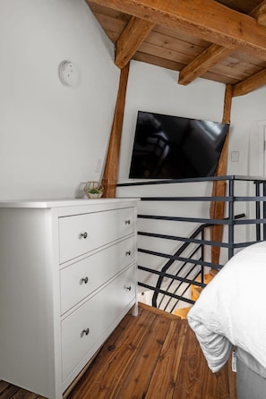 A room with a white dresser, a black metal railing, and a flat-screen TV mounted on the wall.