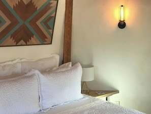 A hotel room with a bed, pillows, a wall-mounted lamp, and a decorative wall piece.