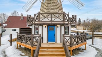 Una estructura de molino con una puerta azul, escaleras de madera y una cerca de metal.