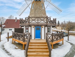 A windmill structure with a blue door, wooden stairs, and a metal fence.