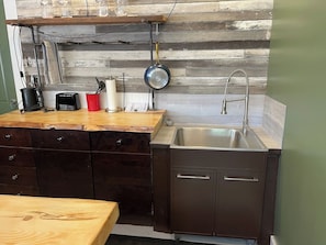 A compact kitchen with a wooden countertop, a stainless steel sink, and a hanging pot rack.