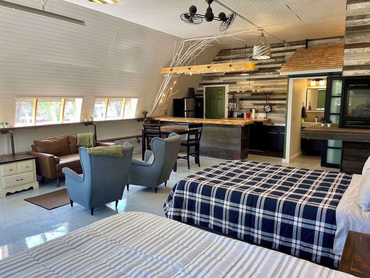 Une chambre spacieuse avec un grand lit, un bureau et une chaise. Il y a également un coin cuisine avec une table et des chaises.