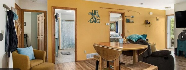 A living room with a wooden dining table, two sofas, a TV, and a wall with a 'Life is better by the lake' sign.