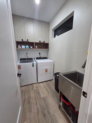 A compact kitchen with a washing machine, a small sink, and a trash bin. - Marvelous 4-bedroom House Near Beaches (Hollywood)