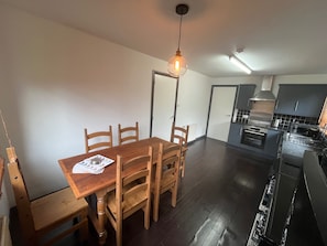 Ein Essbereich mit einem Holztisch und Stühlen, einer Hängeleuchte und Blick in eine Küche mit modernen Geräten.