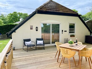 En overdækket terrasse med et træbord og stole, en skydedør samt et lille udendørs siddeområde.