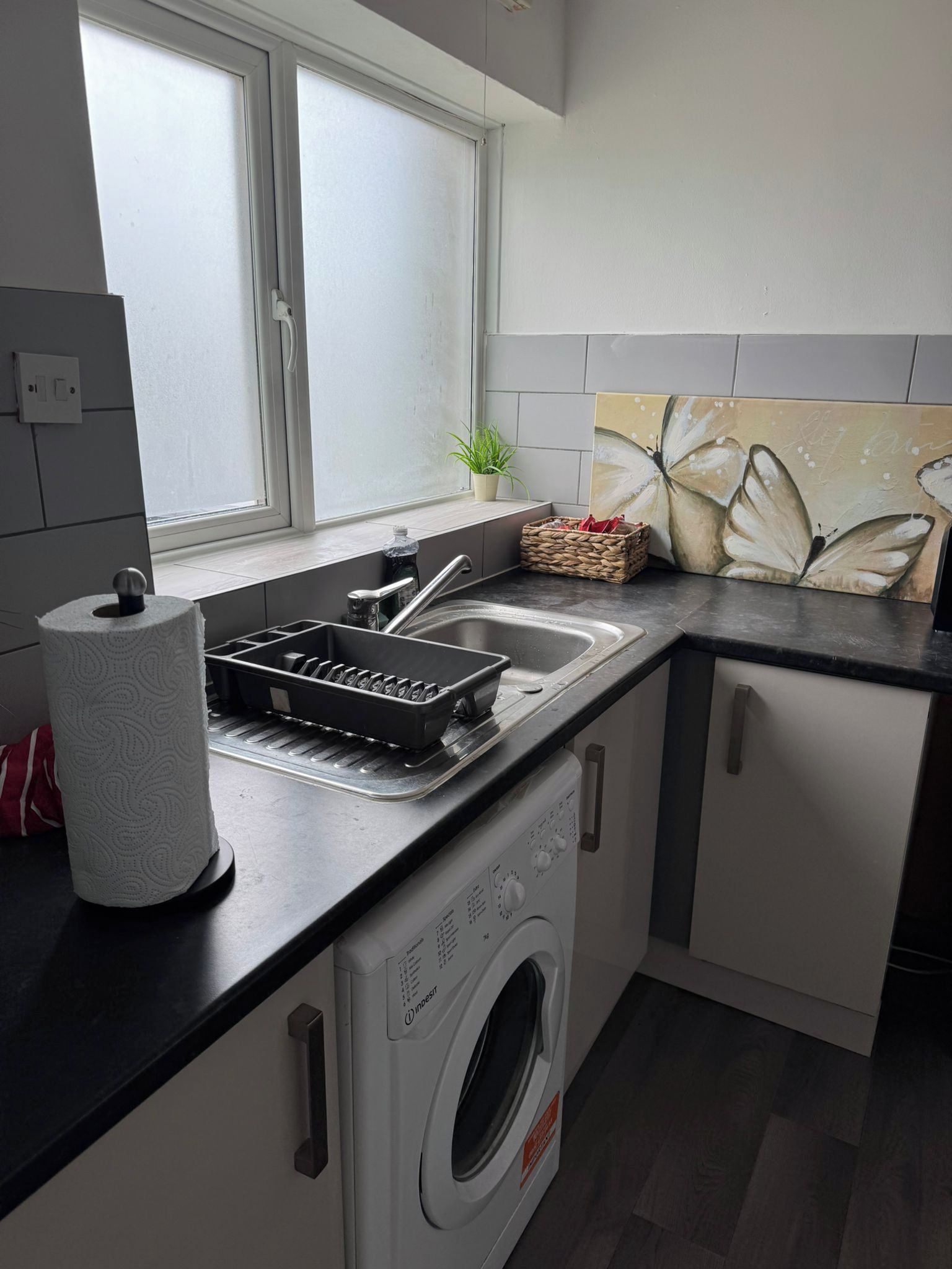 Uma cozinha compacta com máquina de lavar, pia e janela com vidro fosco.