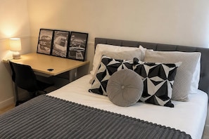 Ein ordentlich eingerichtetes Hotelzimmer mit einem Bett, einem Schreibtisch und einem Stuhl. An der Wand hängen drei gerahmte Bilder.