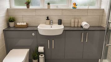 A modern bathroom with a toilet, sink, and shower. There are plants and toiletries on the counter.