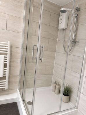 Eine gläserne Dusche mit Duschbrause zum Halten, einer Handbrause und einer wandmontierten Brause.