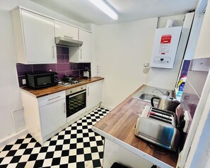 A compact kitchen with white cabinets, a microwave, a gas stove, a toaster, and a sink. - 4-Bed House, Sleeps 9 w Garden & On-Street Parking (Liverpool)