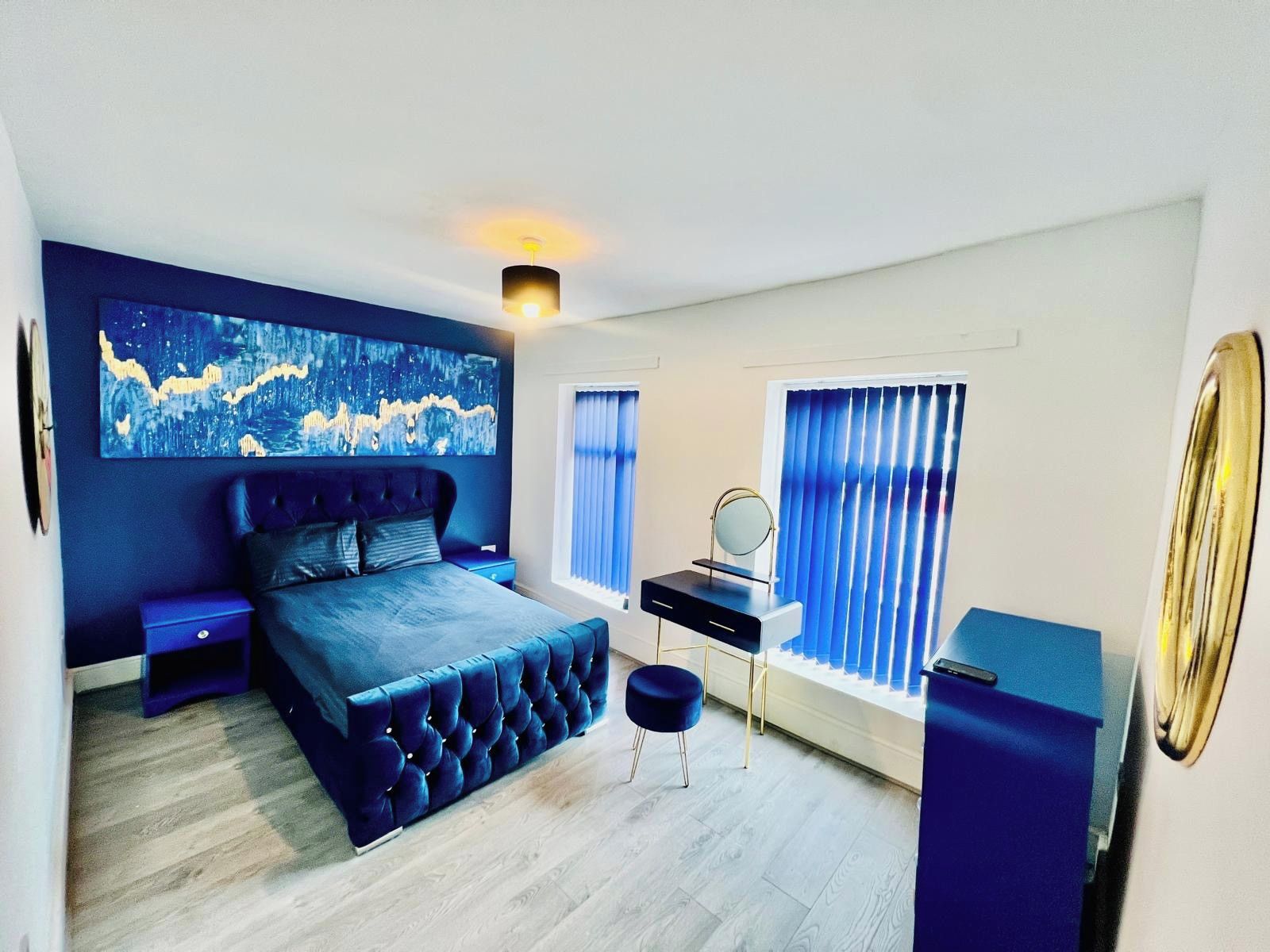 A modern bedroom with a large bed, a bedside table, a dresser, a mirror, and a window with blinds.