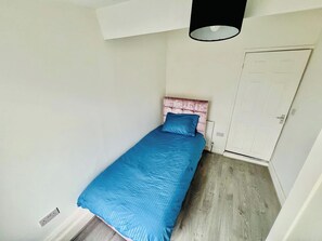 A small, single-bed room with a pink headboard, a blue bedspread, and a white door. - 4-Bed House, Sleeps 9 w Garden & On-Street Parking (Liverpool)