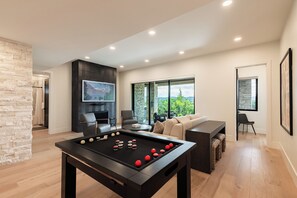 A modern living room with a pool table, comfortable seating, a fireplace, and a large window offering a view. - New Luxury Home in DVE, Private Gym & Hot Tub, Stunning Views (Heber City)