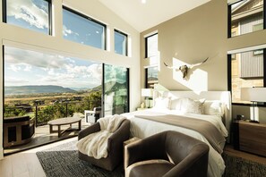 A bedroom with a large bed, a mounted animal skull, and a balcony with a view of the countryside. - New Luxury Home in DVE, Private Gym & Hot Tub, Stunning Views (Heber City)