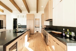 A modern kitchen with wooden cabinets, a black countertop, and stainless steel appliances. - New Luxury Home in DVE, Private Gym & Hot Tub, Stunning Views (Heber City)