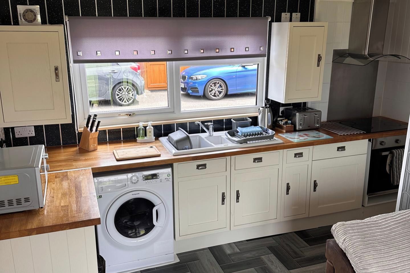 Een kleine keuken met een wasmachine, een spoelbak en een raam met uitzicht op een blauwe auto.
