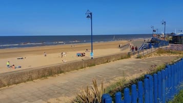 A beach with a paved walkway, a blue fence, and a clear view of the ocean.