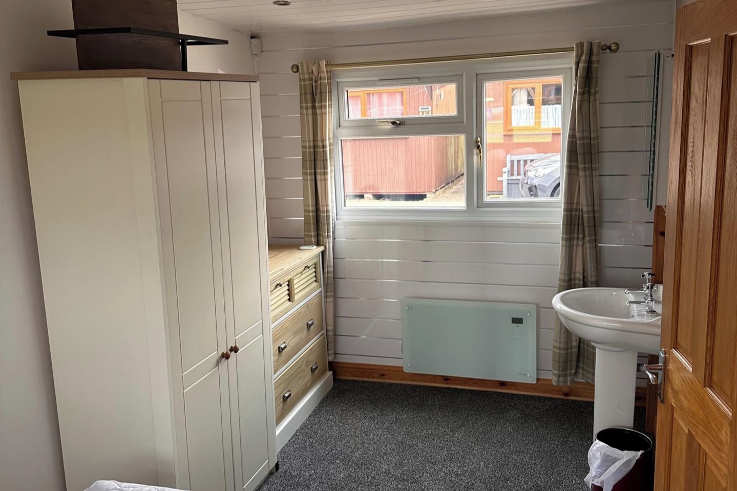 Een kleine badkamer met een wit kastje, een raam met gordijnen, een radiator en een wastafel.