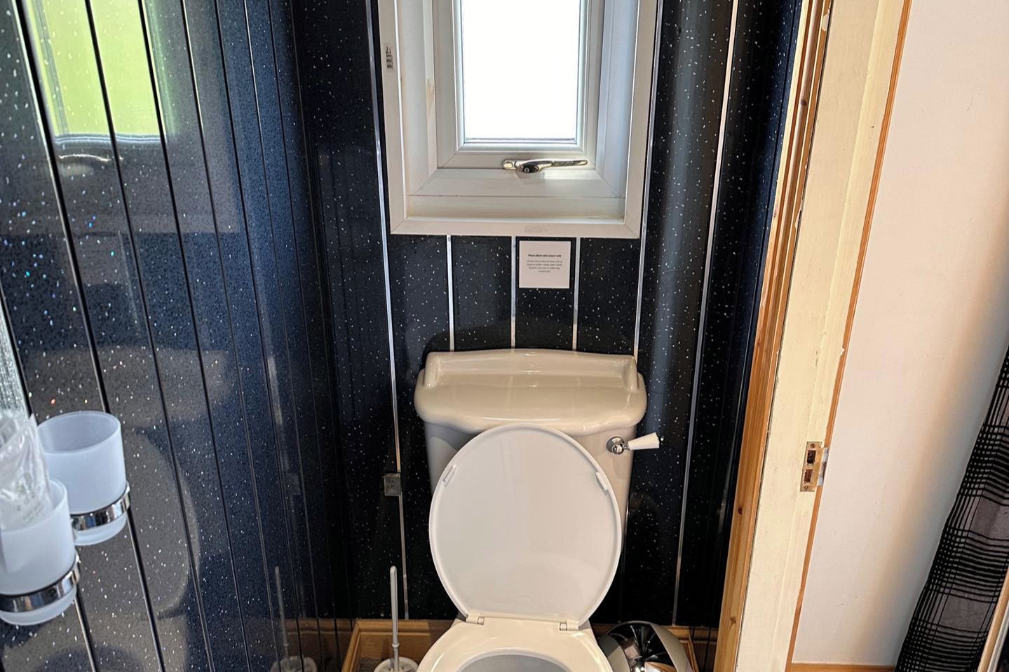 Un baño pequeño y funcional con inodoro, una ventana sobre el lavabo y suelo de madera.
