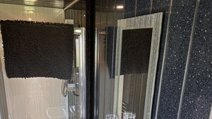 Casa de banho moderna com cabine de duche em vidro, lavatório branco com detalhes em cromo e espelho com moldura decorativa.