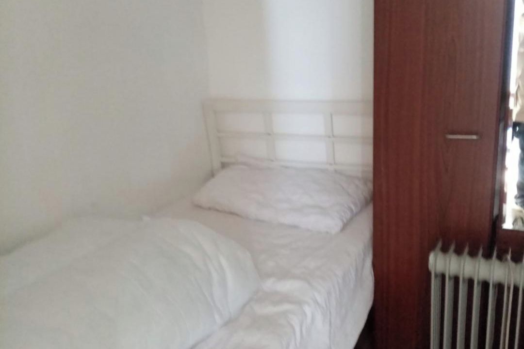 A single bed with a white headboard in a room with white walls and a wooden door.