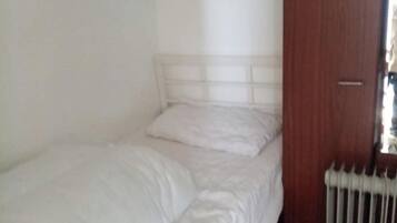 A single bed with a white headboard in a room with white walls and a wooden door.
