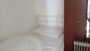 Een eenpersoonsbed met een houten hoofdeinde in een kamer met een radiator en een houten deur.