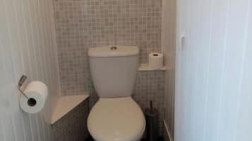 Ein kleines Badezimmer mit Toilette, Toilettenpapier und Bürste.