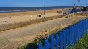 Een strand met een verharde promenade, een blauwe hekken en een helder uitzicht op de oceaan.