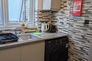 A kitchen with a dishwasher, a kettle, a toaster, and a fire blanket on the wall. - Central Stratford Gem (London)