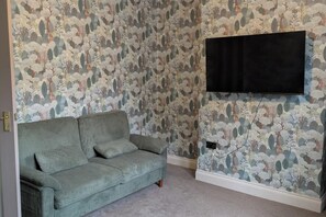 A room with a green sofa, a flat-screen TV mounted on the wall, and a patterned wallpaper. - Central Stratford Gem (London)