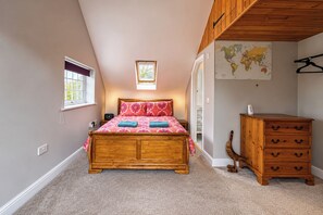 A bedroom with a wooden bed, a dresser, a map on the wall, and a window with a view. - Holdfast Cottage, Sleeps 12 in The New Forest (Bramshaw)