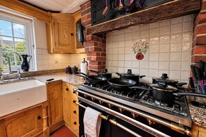 A kitchen with wooden cabinets, a granite countertop, a gas stove, and a window with a view of greenery. - Holdfast Cottage, Sleeps 12 in The New Forest (Bramshaw)