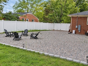 A gravel patio with Adirondack chairs and a white fence.