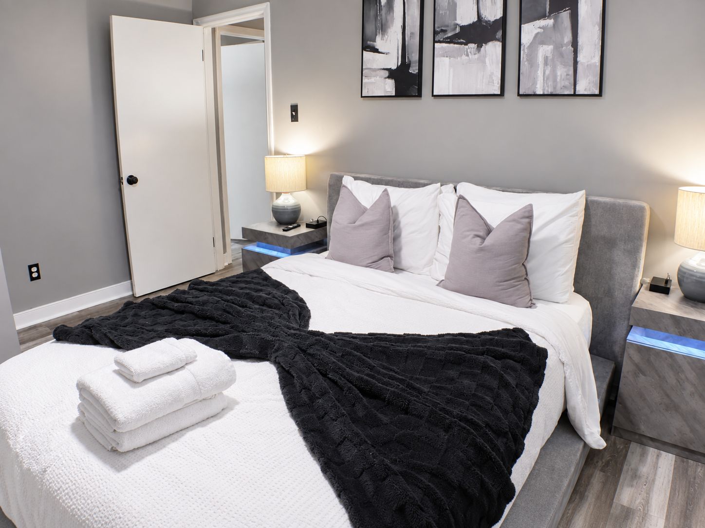 Une chambre d’hôtel avec un lit, des tables de chevet, une lampe, un miroir et des œuvres d’art accrochées au mur.