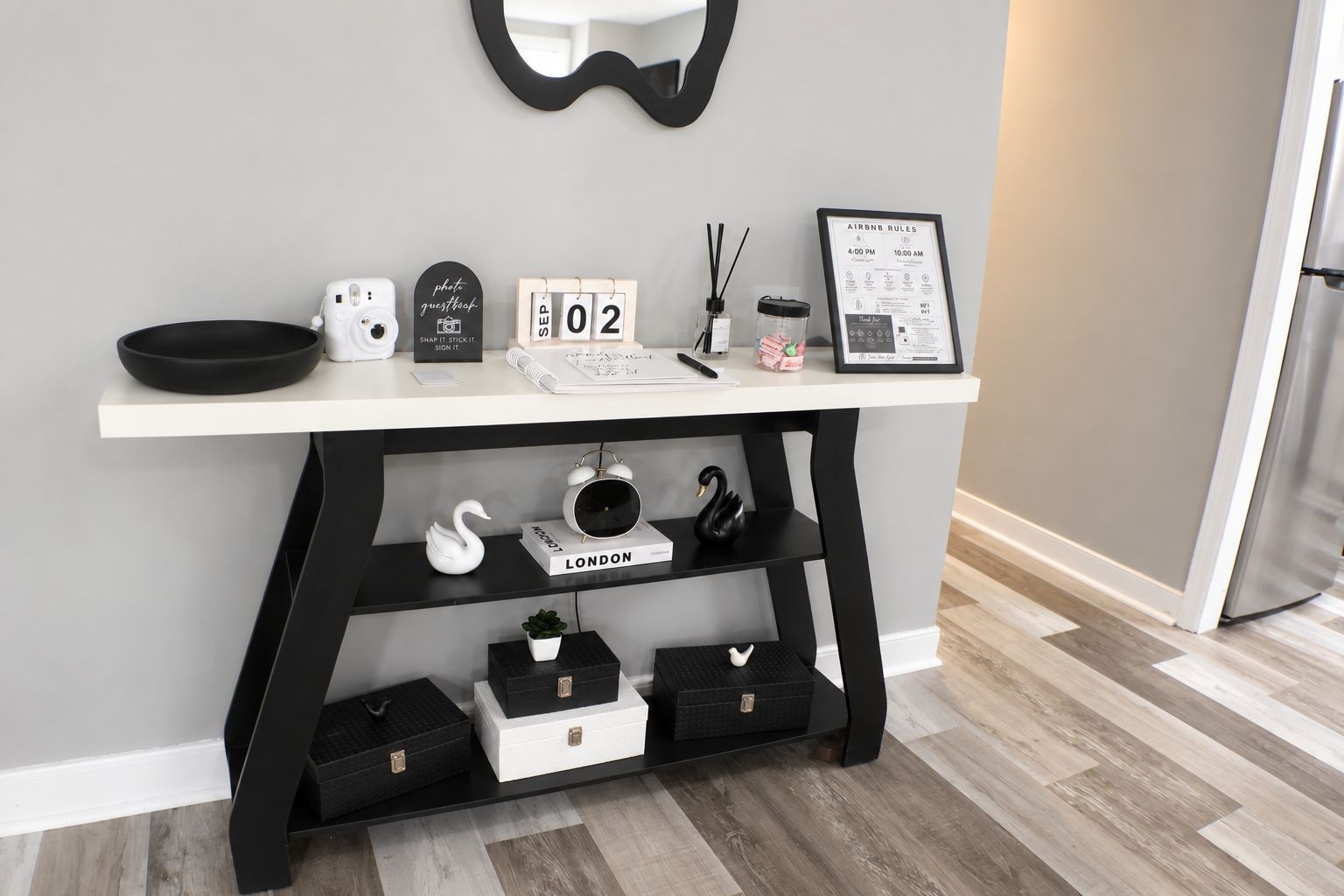 Un bureau blanc avec un cadre noir, un calendrier, un document encadré, un cygne blanc, un cygne noir et un haut-parleur noir.