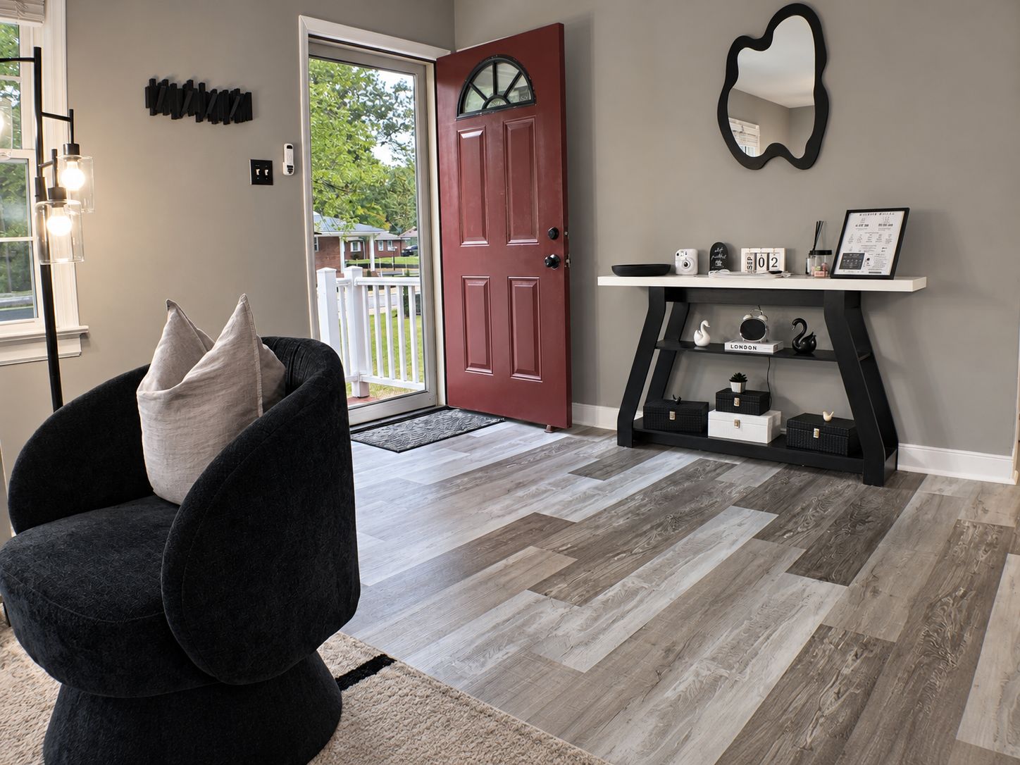 Un salon moderne avec un fauteuil foncé, une porte rouge et une console ornée d’objets décoratifs.
