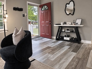 A modern living room with a dark armchair, a red door, and a console table with decorative items.