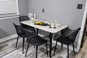 Un comedor con una mesa de mármol, sillas de estructura metálica negra, una botella de vino, copas y una bandeja de frutas.