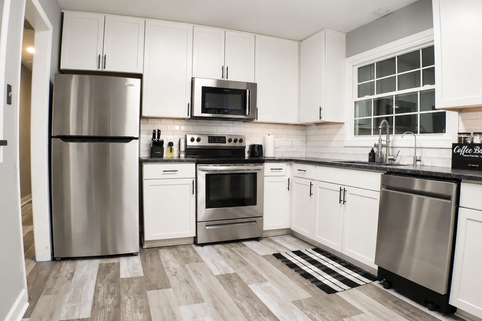 A modern kitchen with stainless steel appliances, white cabinetry, and a herringbone-patterned floor.