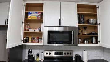 A kitchen with white cabinets, a stainless steel oven, a microwave, and various kitchen utensils.