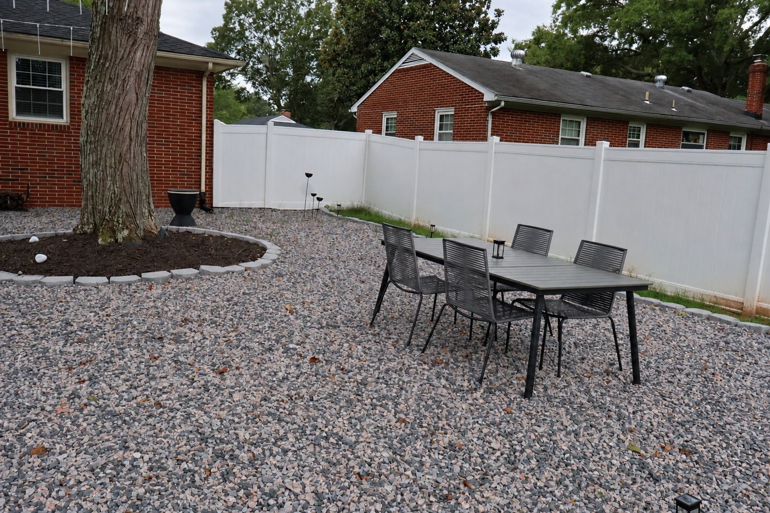 An outdoor patio area with a gravel surface, a table with chairs, and a white fence.