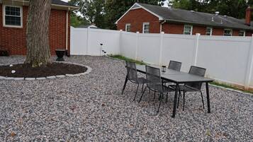An outdoor patio area with a gravel surface, a table with chairs, and a white fence.