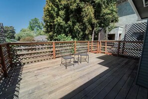 Eine Holzterrasse mit Gitterzaun, zwei Metallstühlen und einem großen Baum im Hintergrund.